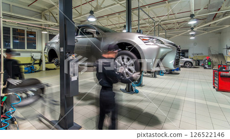 Car mechanic screwing and unscrewing car wheel of lifted automobile at repair service station timelapse hyperlapse 126522146