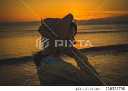 A woman in a straw hat looking at the sea at sunset A woman in a straw hat looking at the sea at sunset 126523798