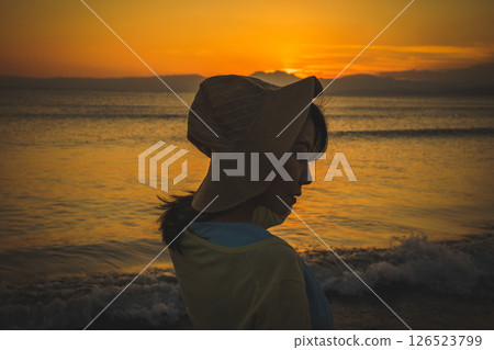 A woman in a straw hat looking at the sea at sunset A woman in a straw hat looking at the sea at sunset 126523799
