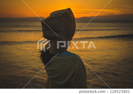 A woman in a straw hat looking at the sea at sunset 126523801