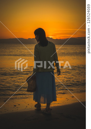 Woman strolling along the beach at sunset 126524089