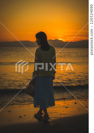Woman strolling along the beach at sunset 126524090