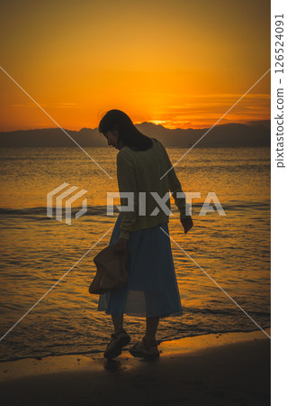 Woman strolling along the beach at sunset 126524091