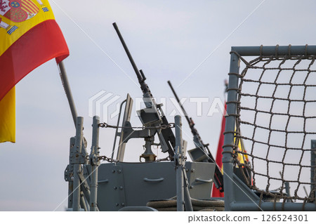 Spanish military ship setup featuring heavy machine guns, safety barriers, and visible Spanish flag signifying maritime defense context Spanish military ship setup featuring heavy machine guns, safety barriers, and visible Spanish flag signifying maritime defense context 126524301
