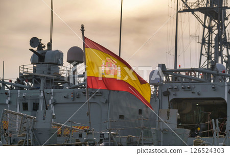 Spanish Navy vessel at sunrise, adorned with a vibrant national flag and equipped for maritime missions Spanish Navy vessel at sunrise, adorned with a vibrant national flag and equipped for maritime missions 126524303