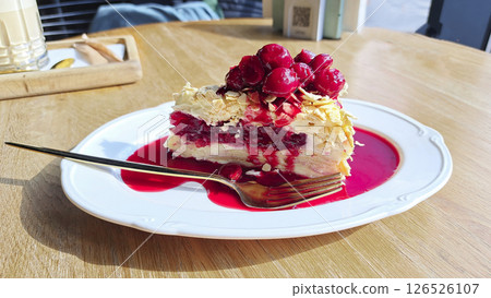 Napoleon pie with cherries and berry sauce on a white plate on a wooden background. Mobile photography Napoleon pie with cherries and berry sauce on a white plate on a wooden background. Mobile photography 126526107