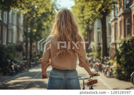 Young woman with long hair riding bicycle on a sunny street surrounded by trees and parked bikes Young woman with long hair riding bicycle on a sunny street surrounded by trees and parked bikes 126526597
