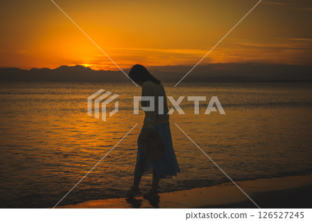 Woman strolling along the beach at sunset Woman strolling along the beach at sunset 126527245