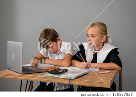Children Schoolwork Homework - Two children in school uniforms sit at a desk doing homework. 126527828