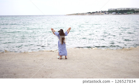 Woman Beach Sea Malta: Joyful woman in dress celebrating at Malta seaside, arms raised, peaceful ocean view. Woman Beach Sea Malta: Joyful woman in dress celebrating at Malta seaside, arms raised, peaceful ocean view. 126527834