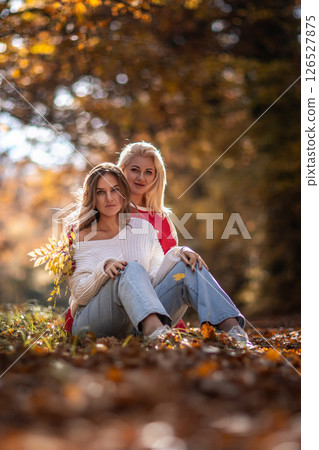 Women Autumn Park Portrait: Friends sitting leaves fall foliage outdoor photoshoot. 126527875