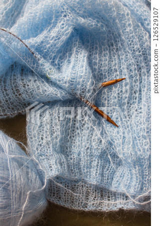 Blue cotton knitting with knitting needles. Soft blue knitwear with wooden circle needles. Knitting pattern background. Knitting lifestyle. Cozy hobby. Warm knitwear. Craft product concept 126529107