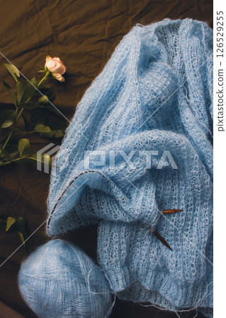 Blue cotton knitting with knitting needles and tiny rose. Soft blue knitwear with wooden circle needles and flower on bed. Knitting lifestyle. Cozy hobby. Craft product concept. Elegant lifestyle. Blue cotton knitting with knitting needles and tiny rose. Soft blue knitwear with wooden circle needles and flower on bed. Knitting lifestyle. Cozy hobby. Craft product concept. Elegant lifestyle. 126529255