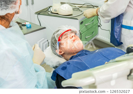 Teen with displeased expression lies in dental chair before oral procedures Teen with displeased expression lies in dental chair before oral procedures 126532027