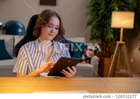 A young woman is using her tablet in a cozy home office, enjoying her work and creativity 126532277