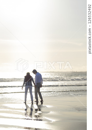 Senior couple holding hands and walking on the beach at sunset 126532492