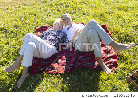Senior couple relaxing on blanket in meadow, enjoying sunny day Senior couple relaxing on blanket in meadow, enjoying sunny day 126532519