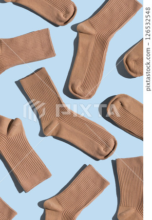 Arrangement of beige socks on light blue surface, highlighting different textures and styles, perfect for fashion, textile design, and creative projects. Vertical 126532548