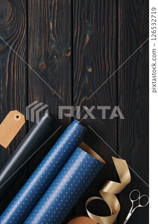 Supplies for gift wrapping. Wrapping paper, tags, and ribbon in blue and gold colors. Wooden background, space for your text. 126532719