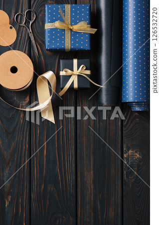 Supplies for gift wrapping. Wrapping paper, tags, and ribbon in blue and gold colors. Wooden background, space for your text. 126532720
