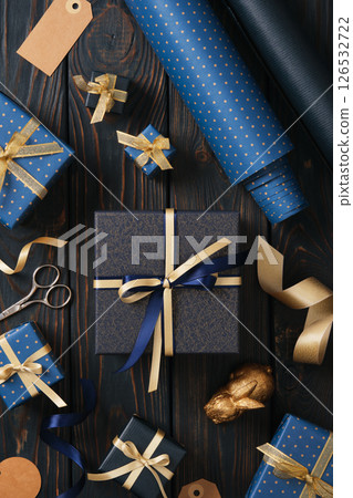 Blue gift box with gold ribbon surrounded by gift wrapping accessories on a blue wooden background 126532722