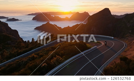 Epic Sunset View in High Mountain Landscape with Motorcycle Driver Riding on Asphalt Road . Pico do Arieiro , Madeira Island . Clouds in the Valley . Epic Sunset View in High Mountain Landscape with Motorcycle Driver Riding on Asphalt Road . Pico do Arieiro , Madeira Island . Clouds in the Valley . 126532768