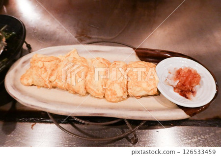 close up of Japanese pan fried egg omelette rolls (Tamagoyaki) cut into pieces on a white plate with sauce on the side 126533459