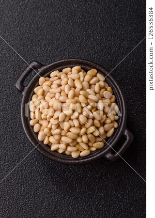 Peeled pine nuts in a bowl on a dark concrete background 126536384