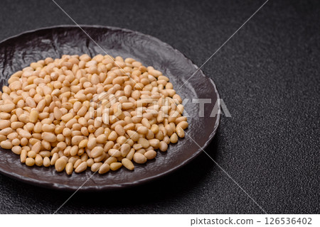Peeled pine nuts in a bowl on a dark concrete background Peeled pine nuts in a bowl on a dark concrete background 126536402