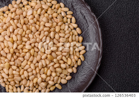Peeled pine nuts in a bowl on a dark concrete background 126536403