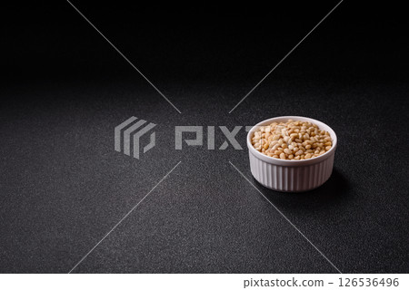 Peeled pine nuts in a bowl on a dark concrete background 126536496
