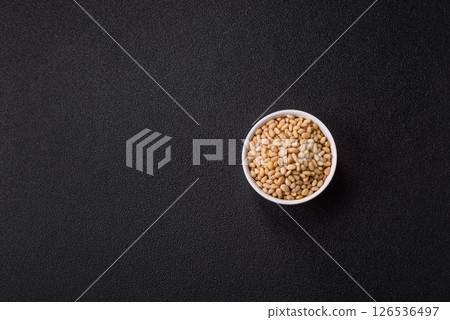 Peeled pine nuts in a bowl on a dark concrete background 126536497