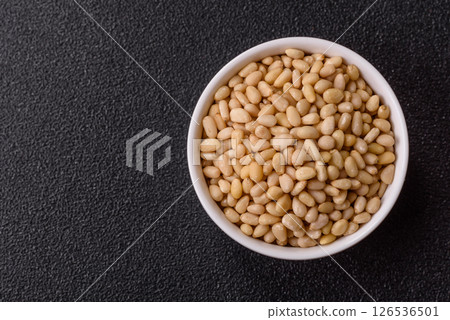 Peeled pine nuts in a bowl on a dark concrete background 126536501