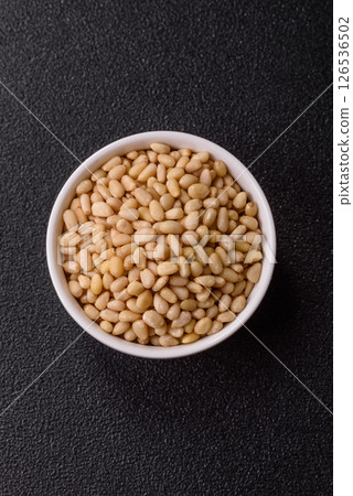 Peeled pine nuts in a bowl on a dark concrete background Peeled pine nuts in a bowl on a dark concrete background 126536502