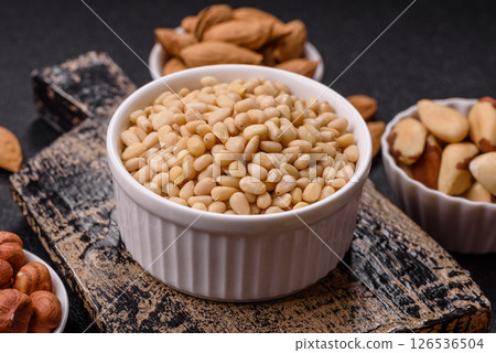 Peeled pine nuts in a bowl on a dark concrete background 126536504