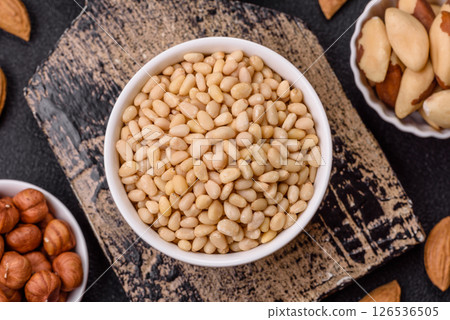 Peeled pine nuts in a bowl on a dark concrete background Peeled pine nuts in a bowl on a dark concrete background 126536505