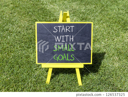 Start with small goals symbol. Concept words phrase Start with small goals on beautiful black blackboard. Beautiful green grass lawn background. Business Start with small goals concept. Copy space. 126537325