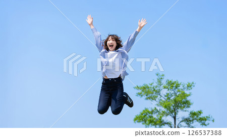 A woman jumping energetically into the blue sky 126537388