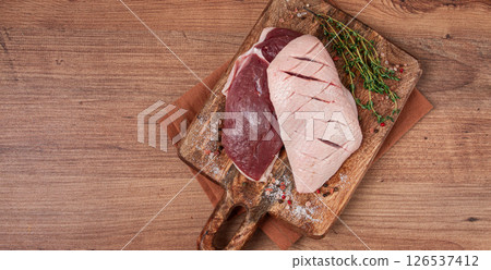Fresh raw duck breasts, on a wooden chopping board, with herbs and spices, no people 126537412