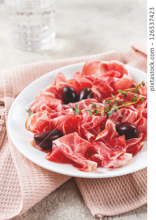 Freshly cut dried meat, served with olives and herbs, on a white plate, light background, no people, 126537423