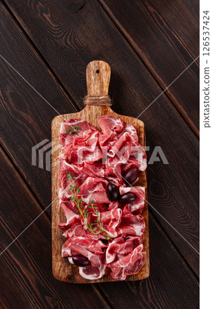 Freshly cut dried meat, served with olives and herbs, on a wooden chopping board, no people, 126537424