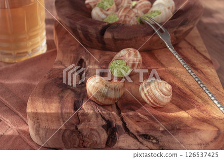 Snails cooked with herb oil on a wooden plate, served with white wine, natural light, no people, 126537425