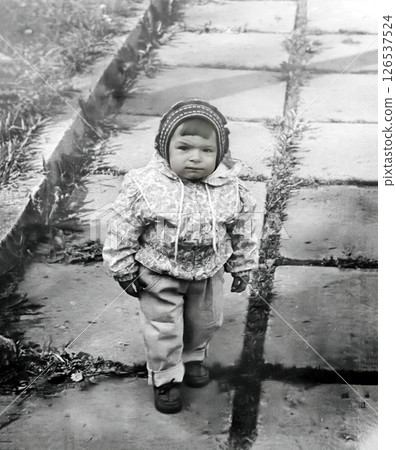 Vintage portrait of a little serious girl walking along a path in the park in spring. Retro photo 1995. 126537524
