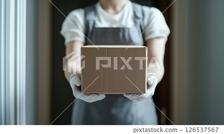 Hands of a delivery person handing over a package at the front door 126537567