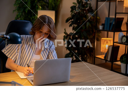 A Focused Young Woman Engaged in Working on Her Laptop in a Modern Home Office Environment 126537775