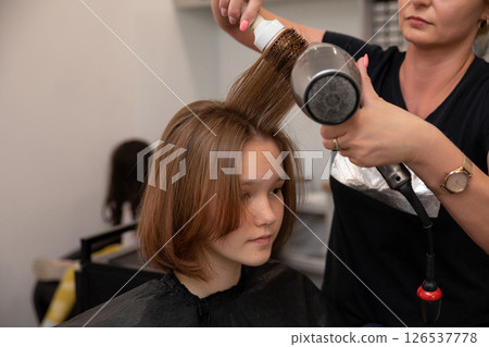 A dedicated hair stylist is skillfully using a blow dryer on a young client inside a salon A dedicated hair stylist is skillfully using a blow dryer on a young client inside a salon 126537778