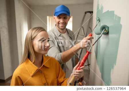 Couple painting wall together in new home using paint roller Couple painting wall together in new home using paint roller 126537964