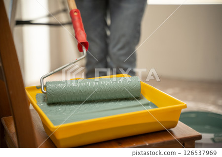 Painter dipping paint roller in tray with green paint during home renovation Painter dipping paint roller in tray with green paint during home renovation 126537969