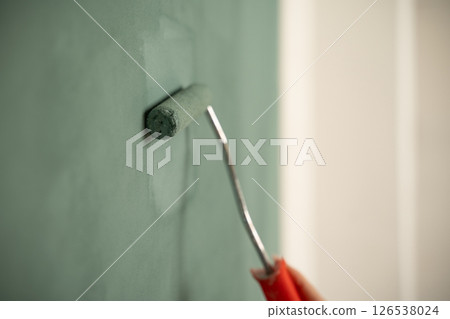Painter applying green paint on wall with roller 126538024