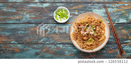 Dan dan noodles served with chopsticks and green onions top view on rustic wooden table, traditional Chinese Sichuan dish Dan dan noodles served with chopsticks and green onions top view on rustic wooden table, traditional Chinese Sichuan dish 126538112